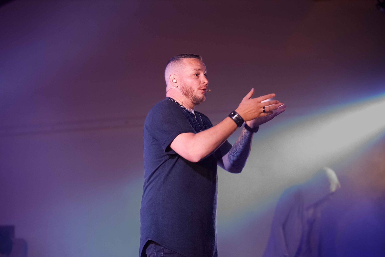 R'Key explique au public, la main tendue, dans la lumière des projecteurs