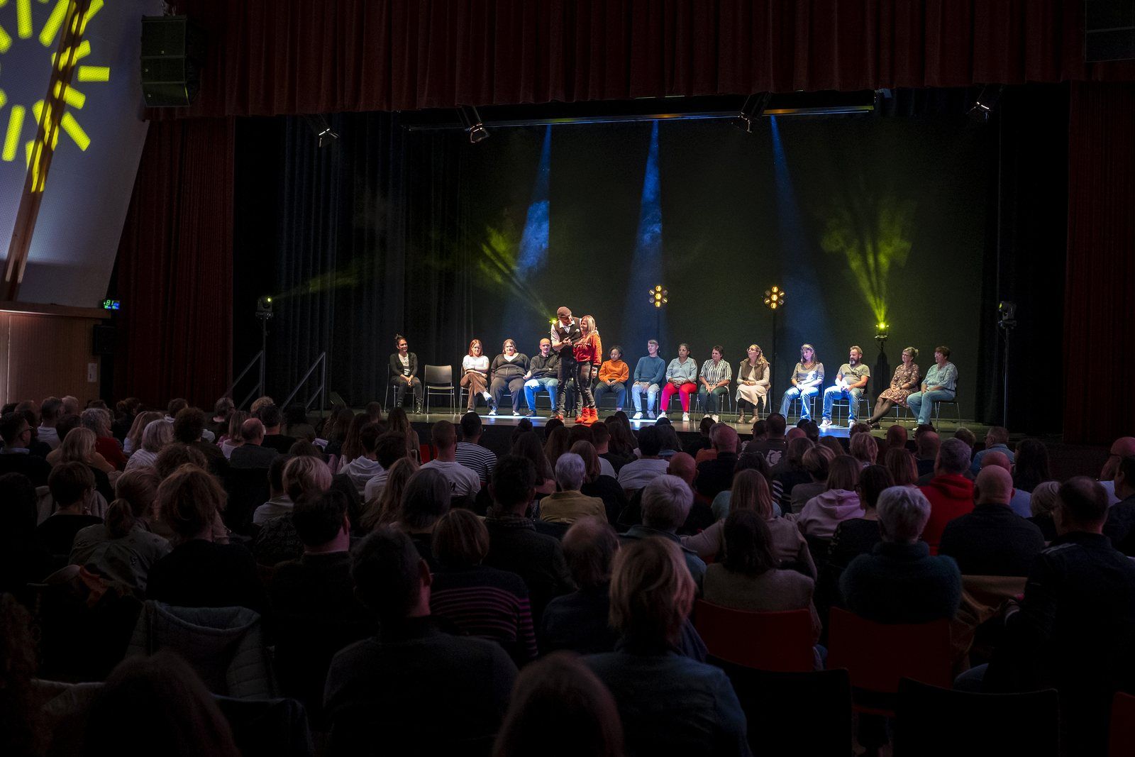 Une salle comble face à la scène où les volontaires sont assis en ligne pendant un spectacle d'hypnose en Alsace